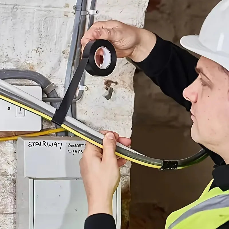 Electricista con casco usando cinta aislante negra para fijar cables eléctricos a la pared